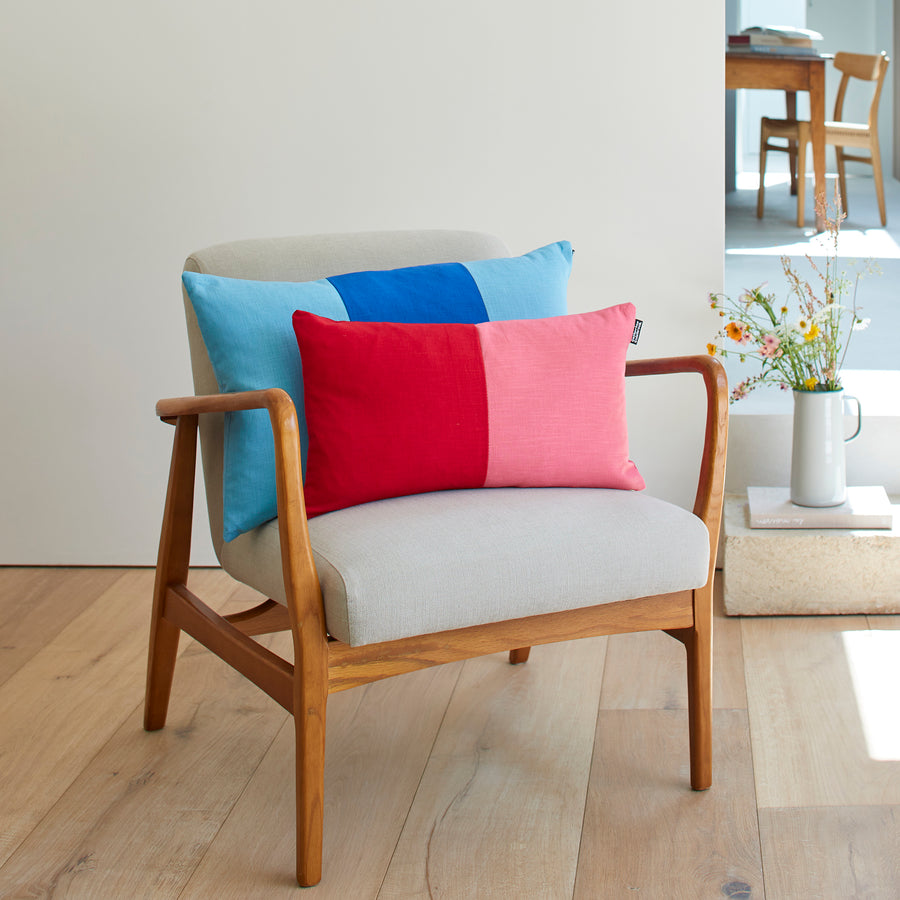 CATHERINE COLEBROOK DOUBLE COLOUR BLOCK CHERRY ROSE CUSHION AND THE TRIPLE COLOUR BLOCK DENIM AZURE CUSHION ON A CHAIR